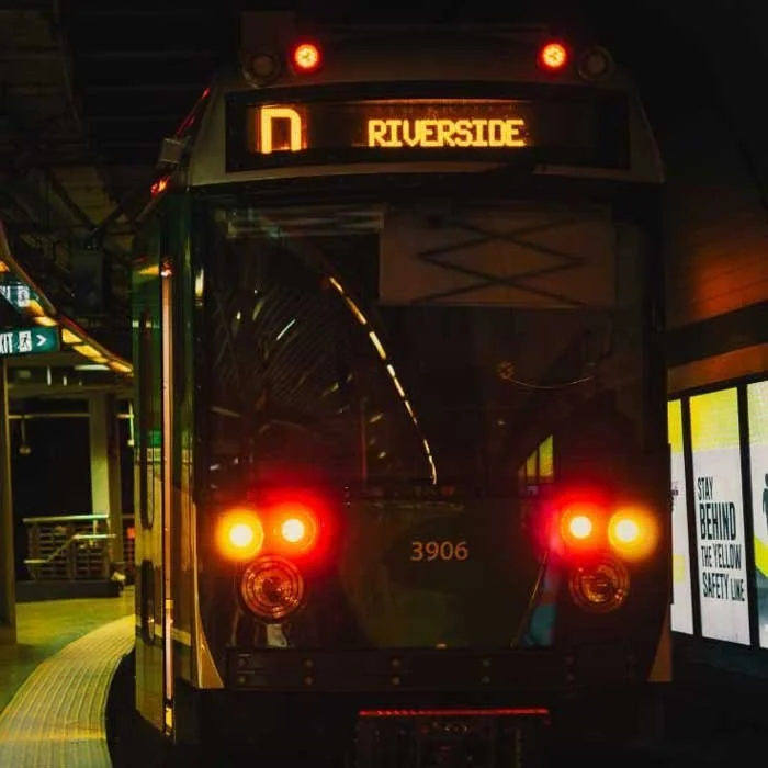Front view of a train car at a station with a display reading "Riverside". The train is illuminated with red lights and numbered 3906.