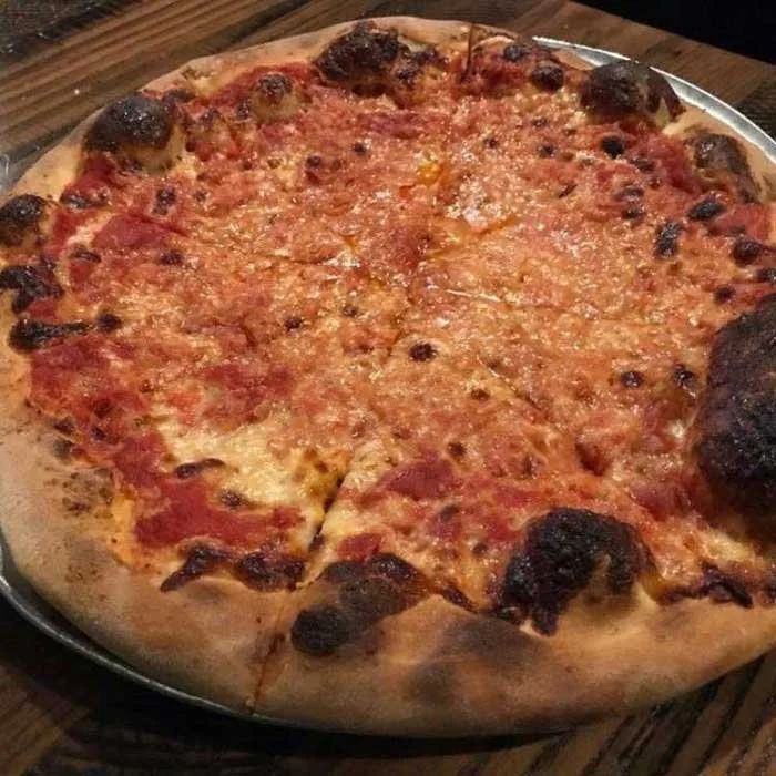 A cheese pizza with a slightly burnt crust on a wooden table.